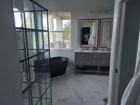 Bathroom with a black bathtub, gray vanity, and large window.