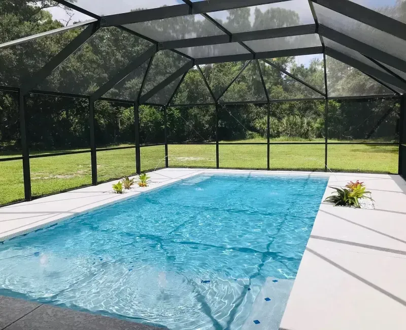 Pool enclosed in a screened structure with white decking, and lush green lawn and trees in the background.