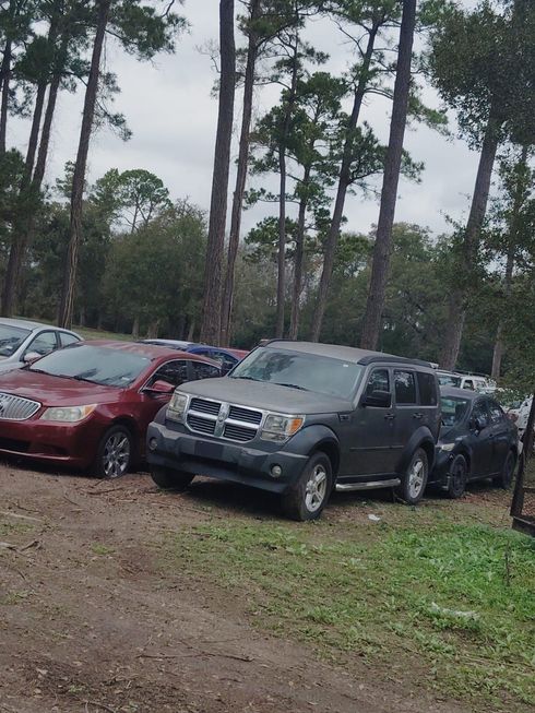 Gray Dodge Nitro SUV parked in a dirt lot among other cars and trees.
