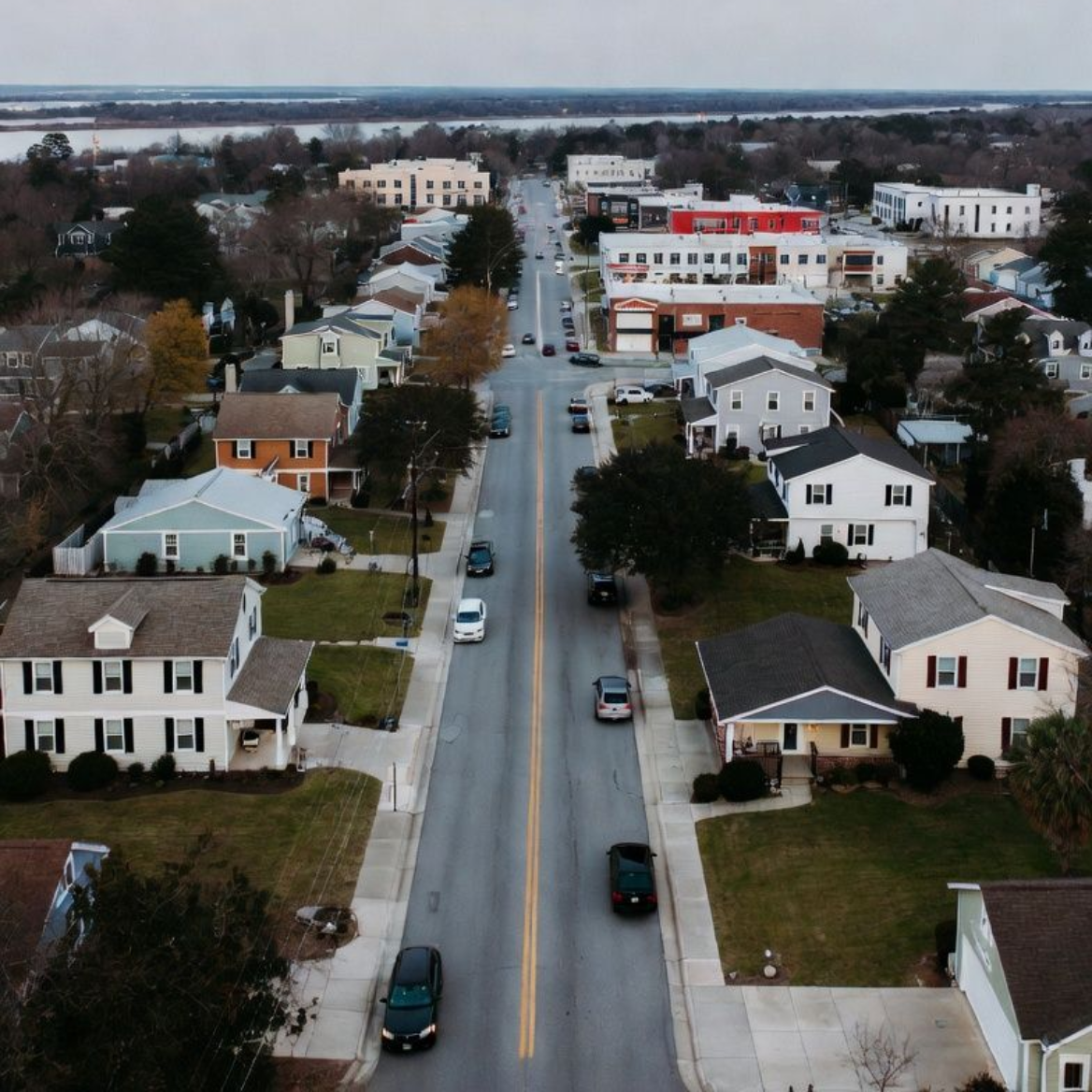 Aerial view of a street in a small town lined with houses, leading to a downtown area.