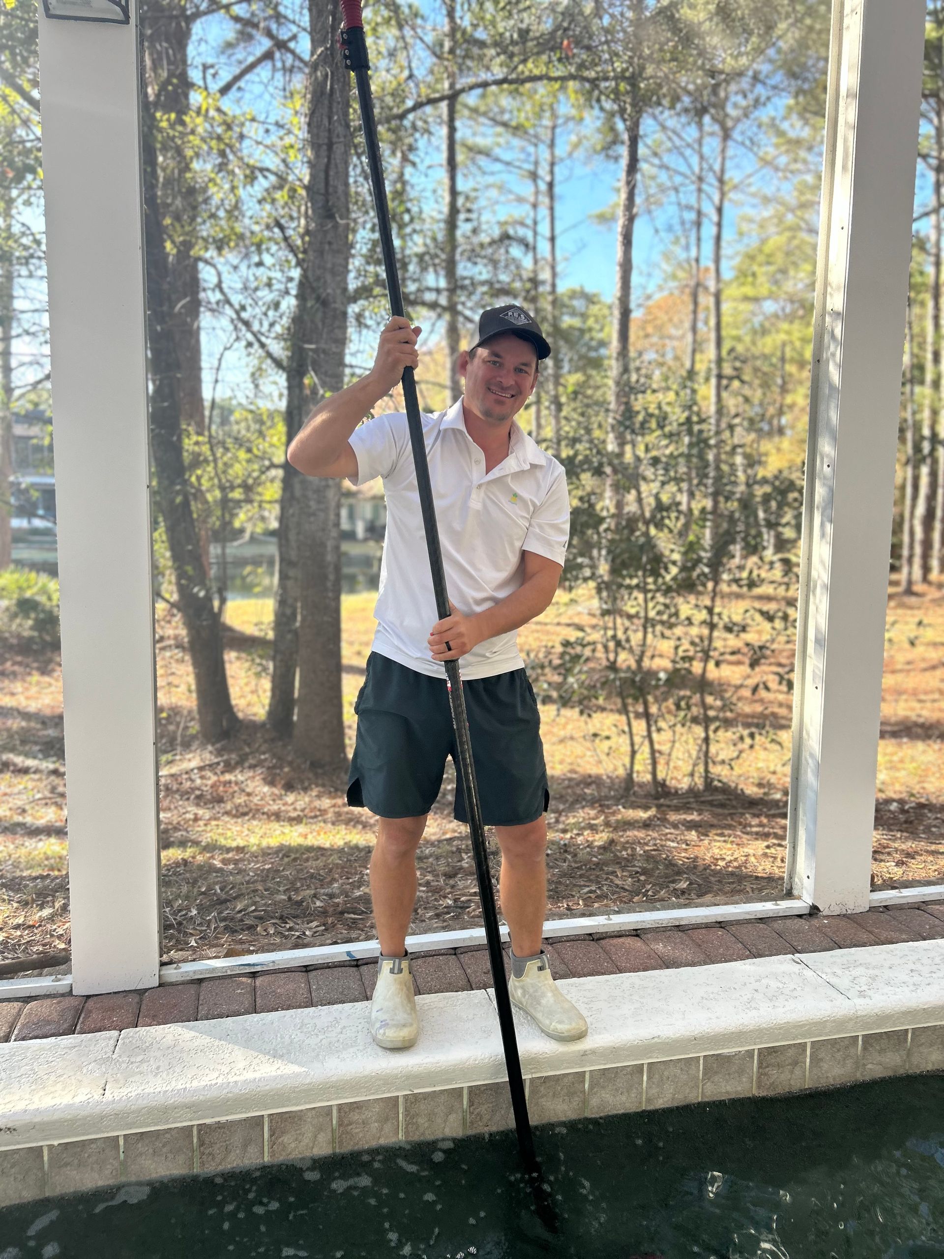A man is standing next to a pool holding a pole.