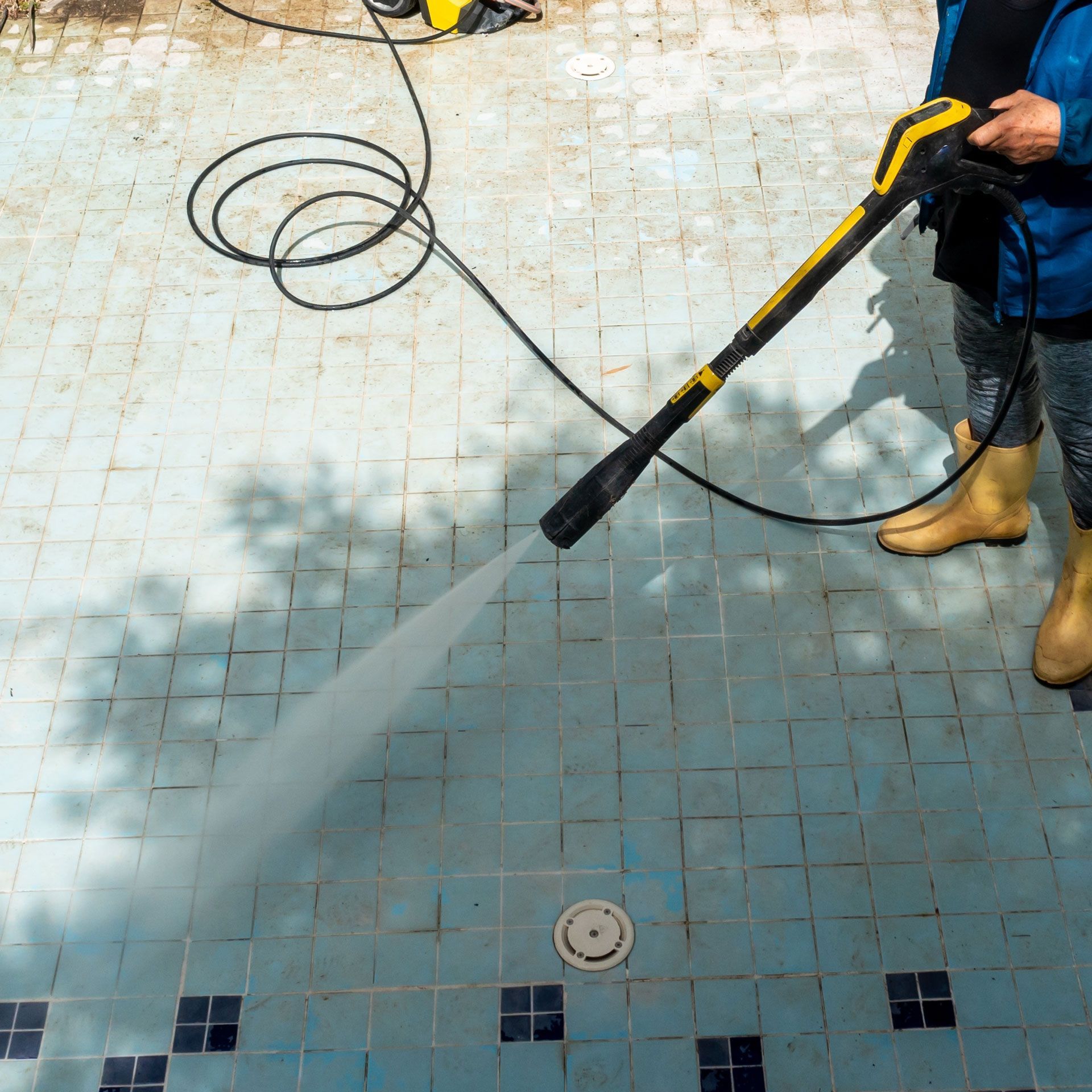 A man is cleaning a swimming pool with a high pressure washer.