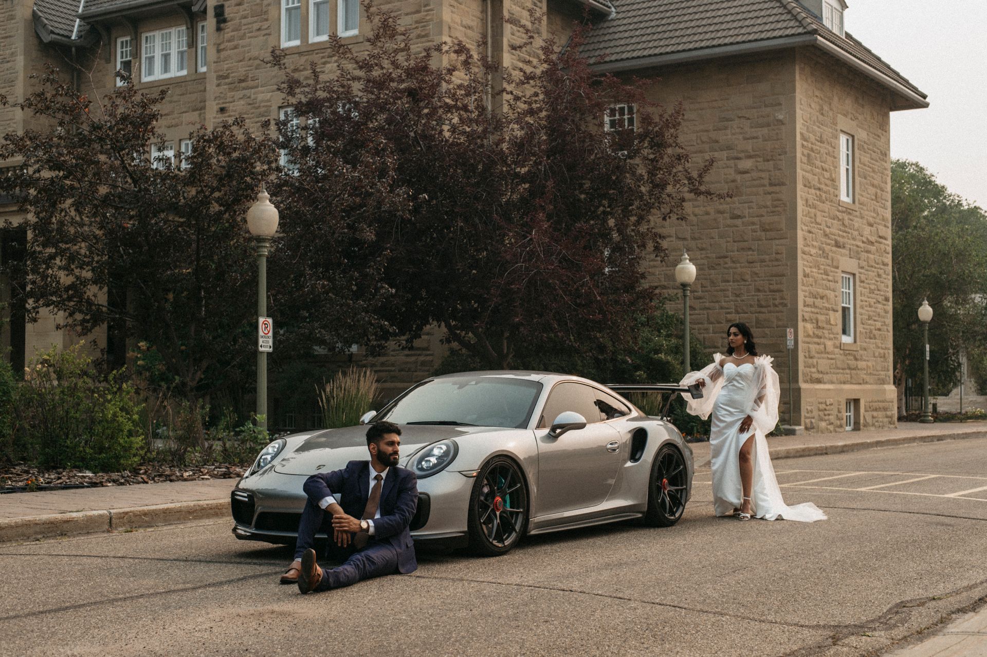 A bride and groom are posing for a picture next to a sports car.