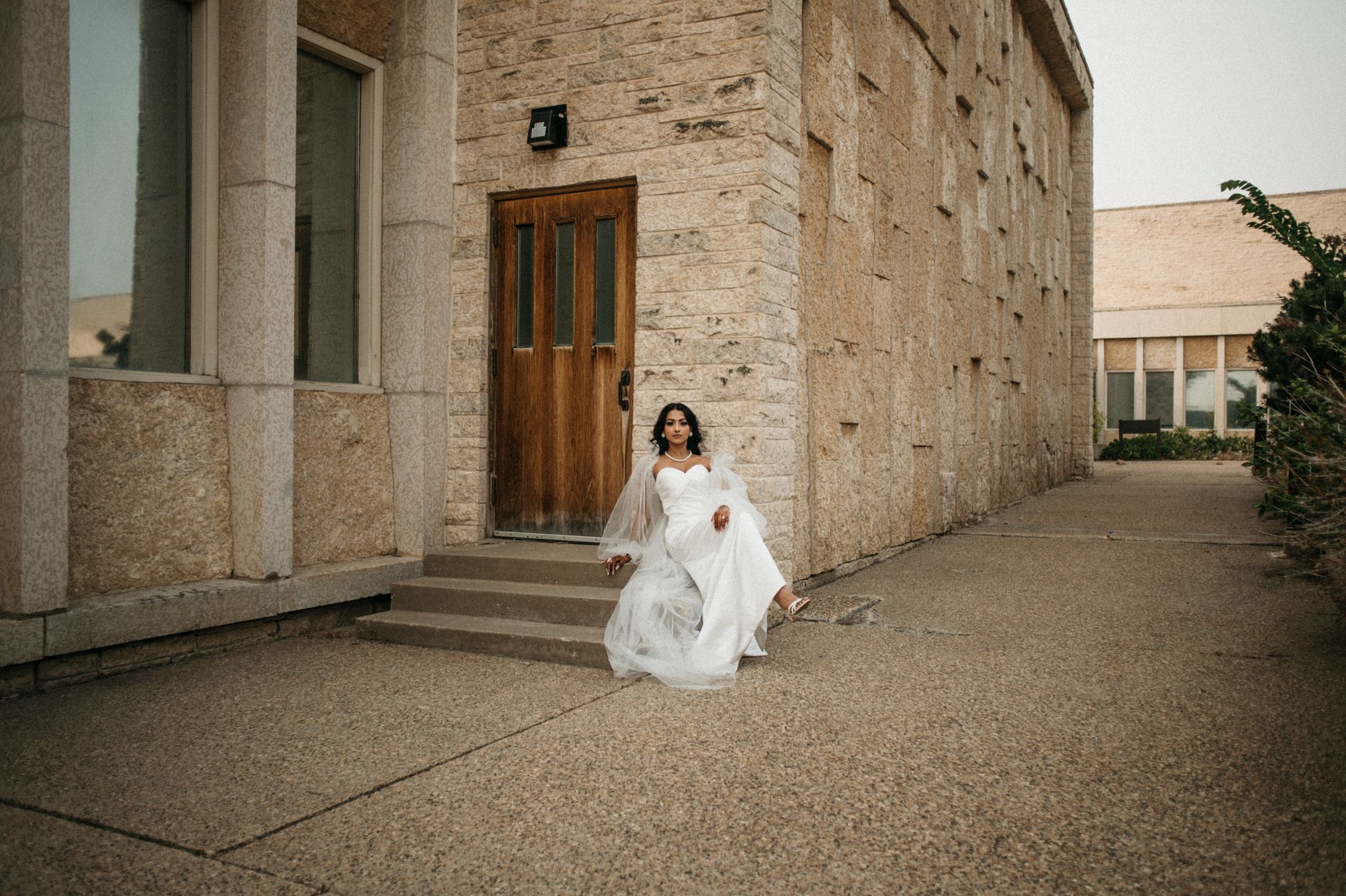 A bride in a wedding dress is sitting on the steps of a building.