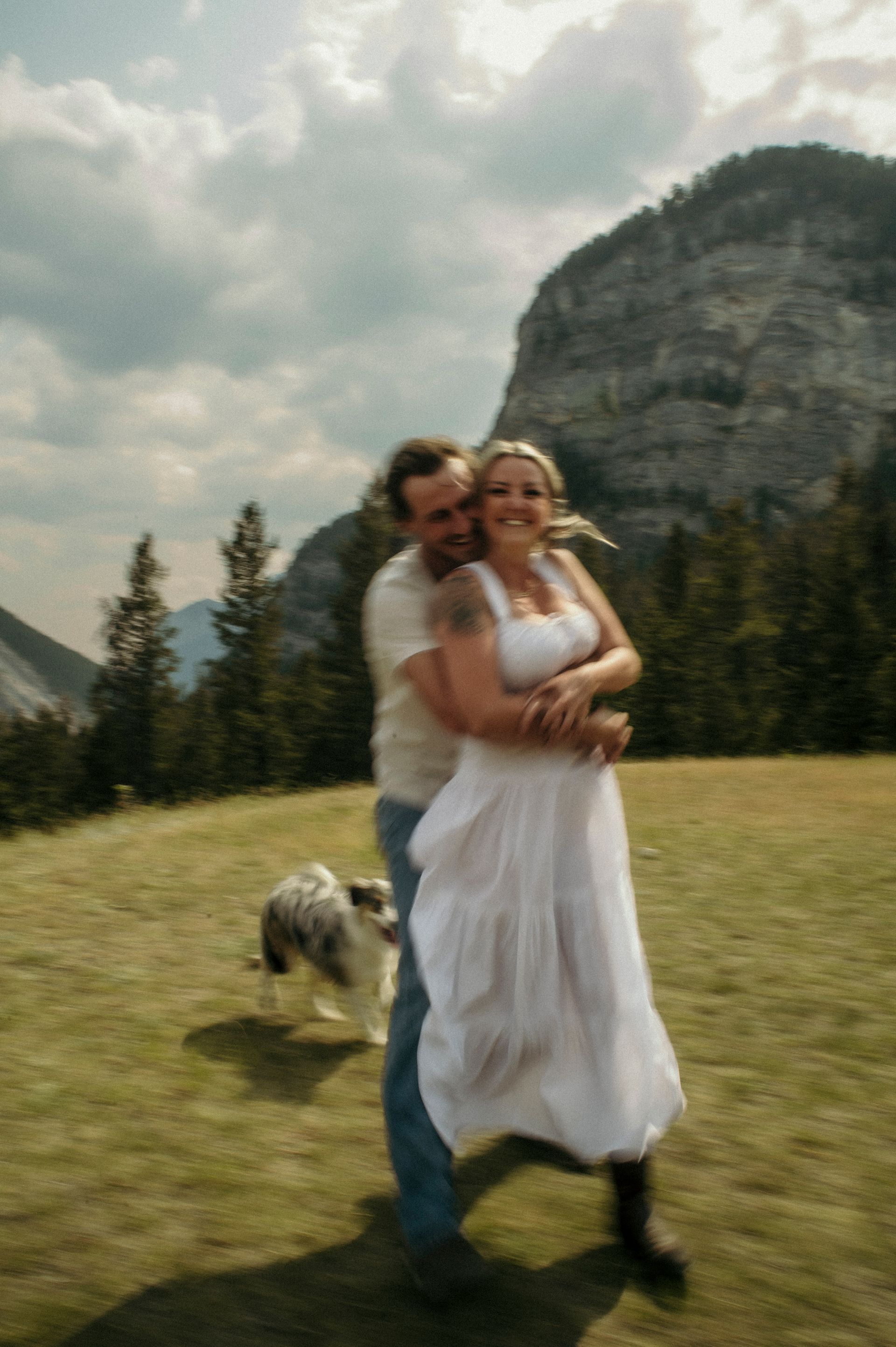 A man and woman are hugging in a field with a dog.