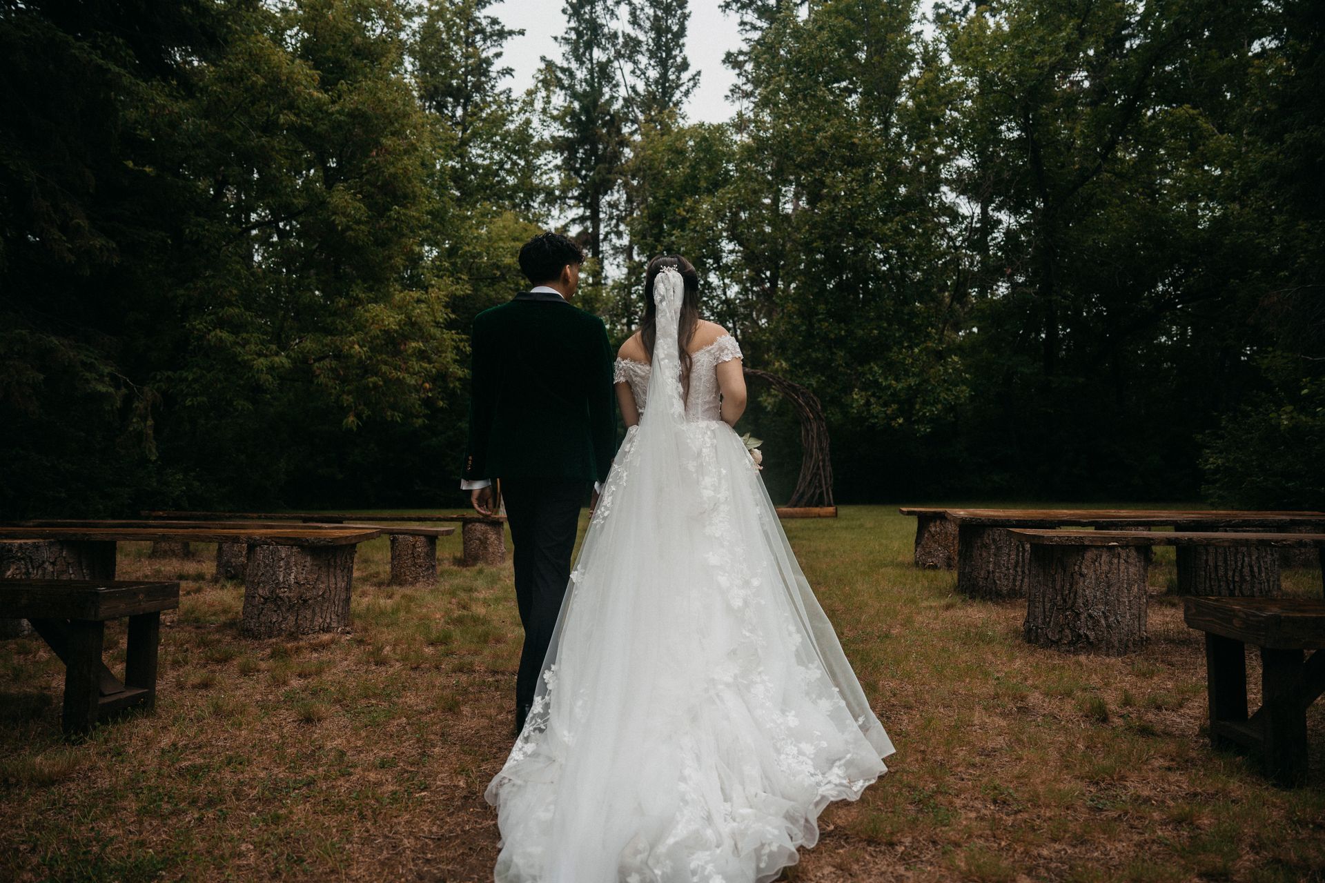 A bride and groom are walking through a forest.
