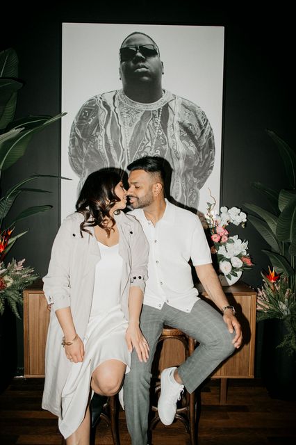 A man and a woman are kissing in front of a painting of a man.