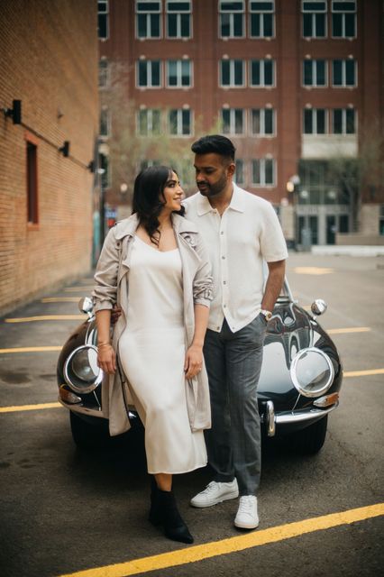 A man and a woman are standing next to a car in a parking lot.