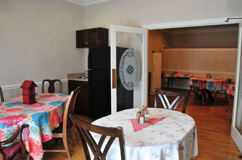 Interior view of a kitchen and dining area with colorful tablecloths, a black refrigerator, and a doorway.