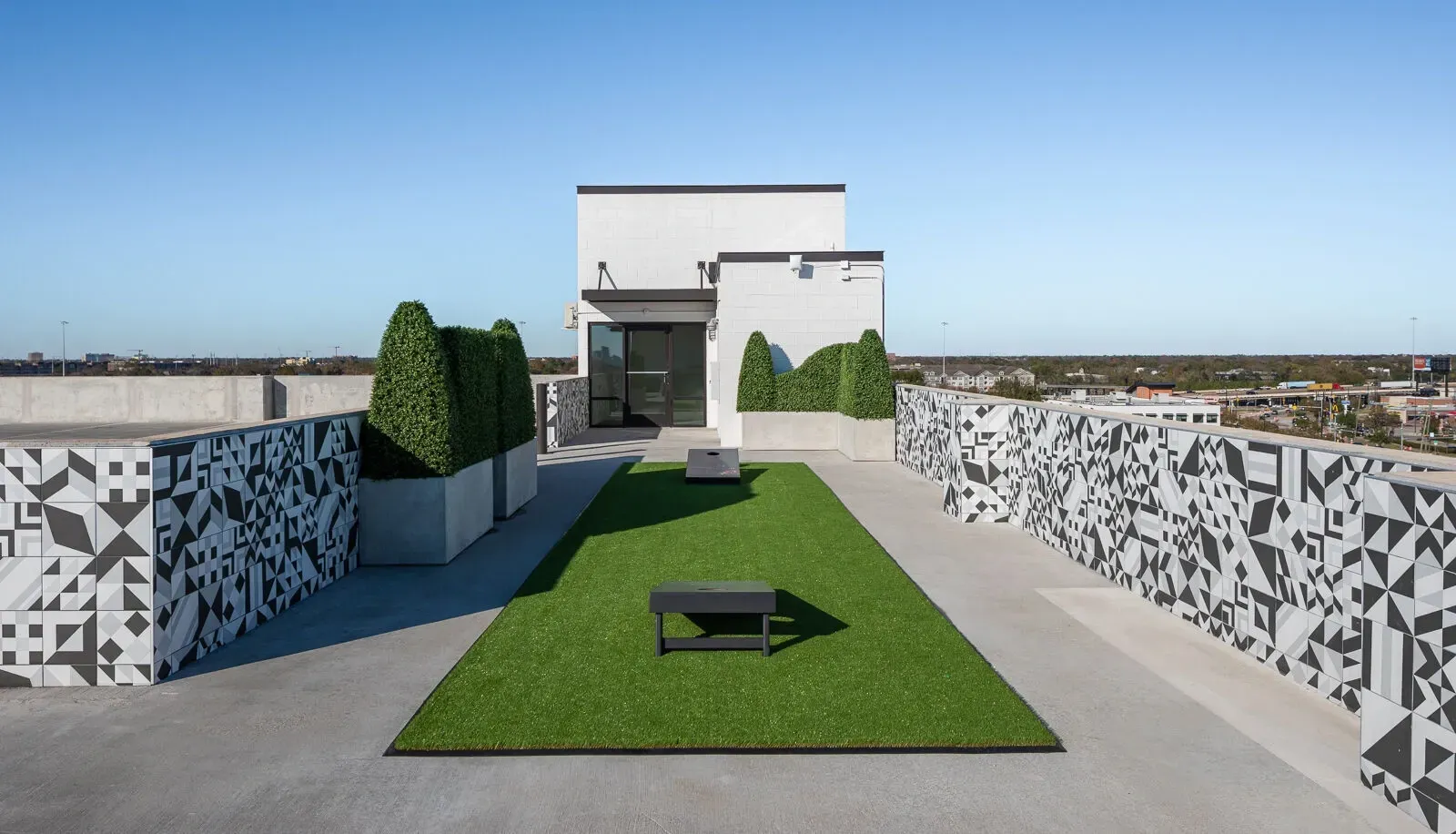 Rooftop terrace with a green lawn strip, bench, and patterned walls under a clear blue sky