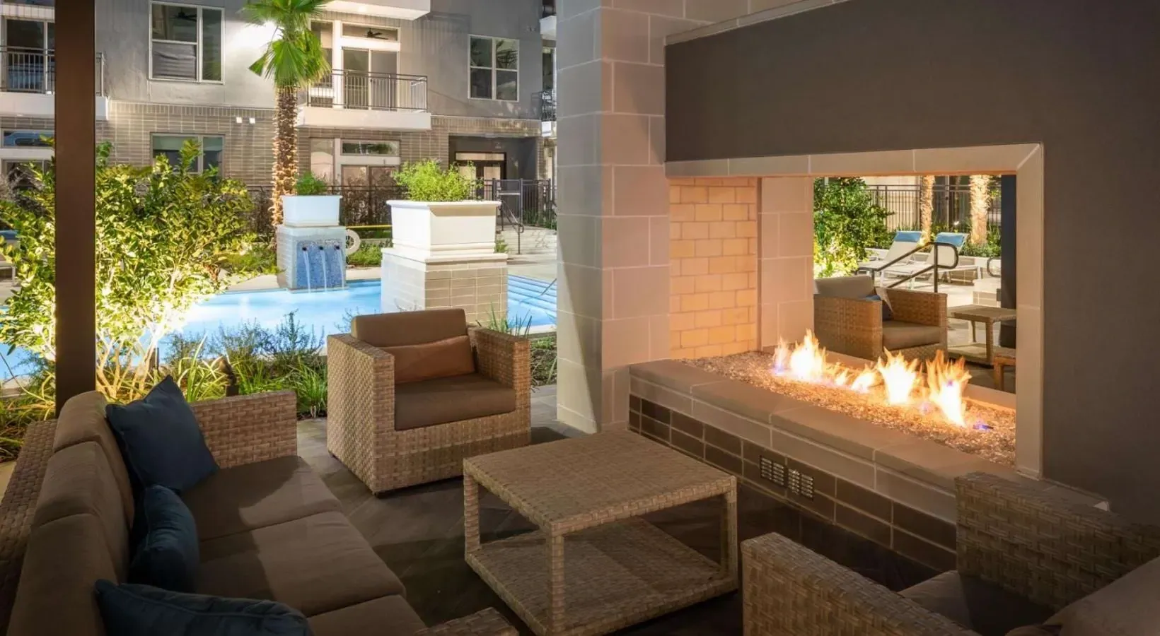 Outdoor lounge area with a modern gas fireplace and seating, overlooking a swimming pool.