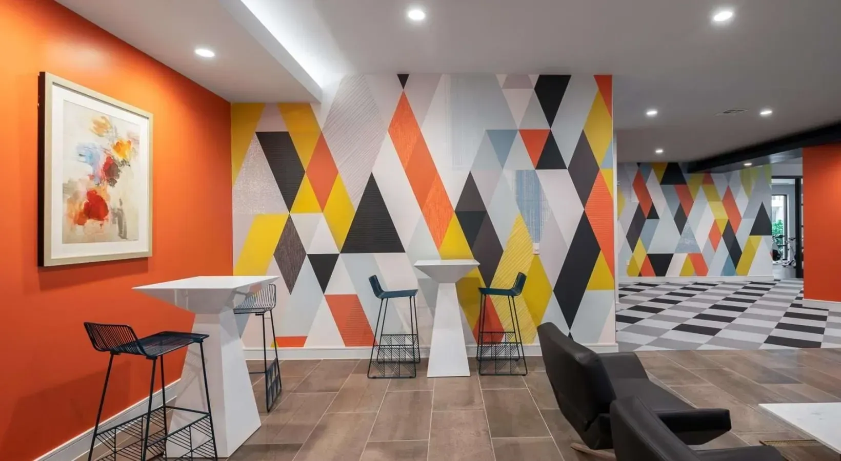 Modern lounge area with colorful geometric accent wall, bar stools, and tables.