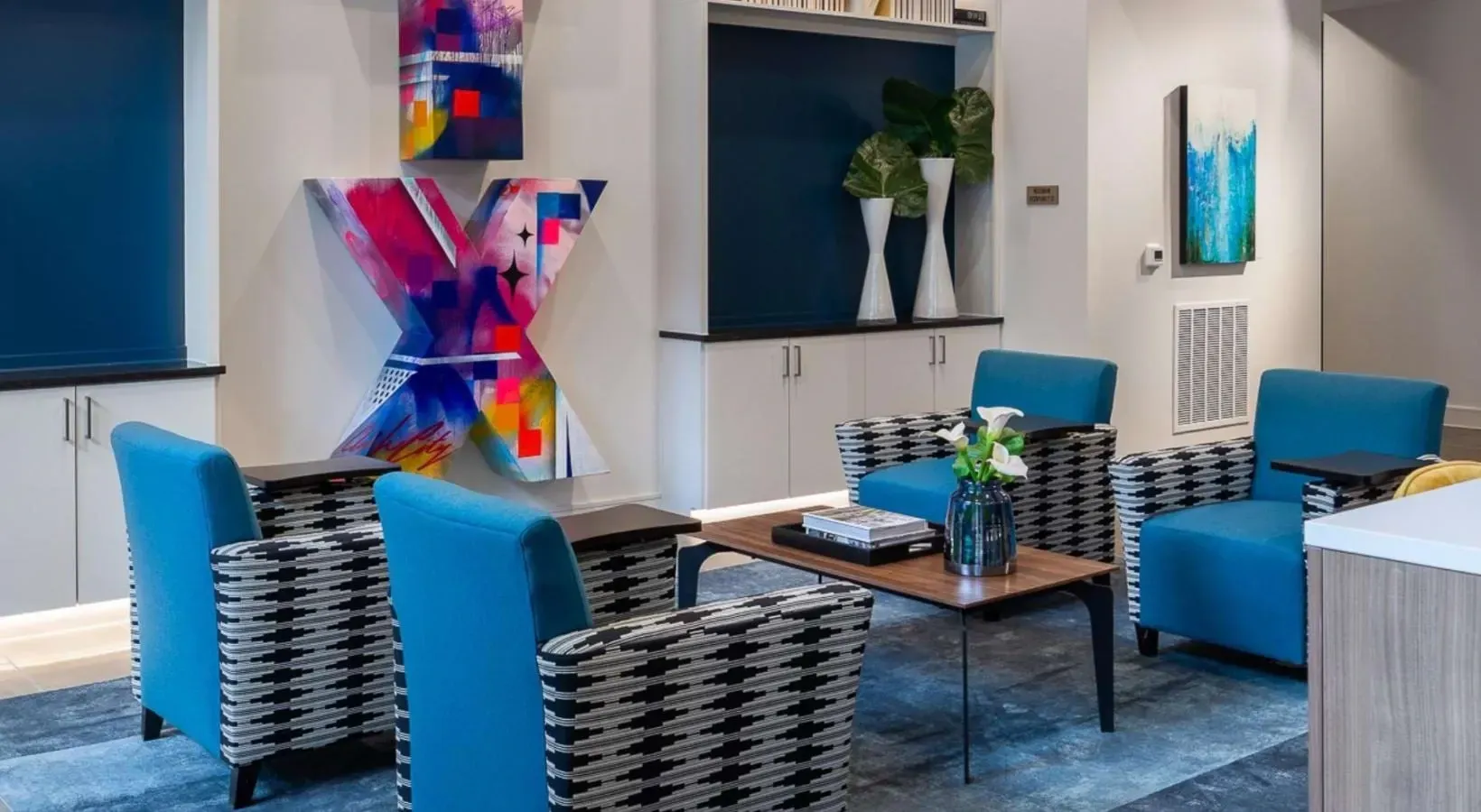 Lounge area with blue chairs, modern art, and decorative vases.
