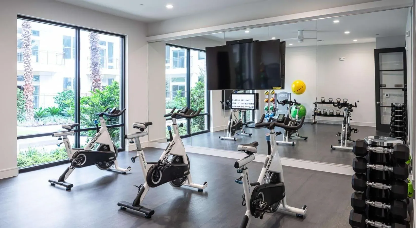 Spinning bikes and weights in a well-lit fitness center with large mirrors.