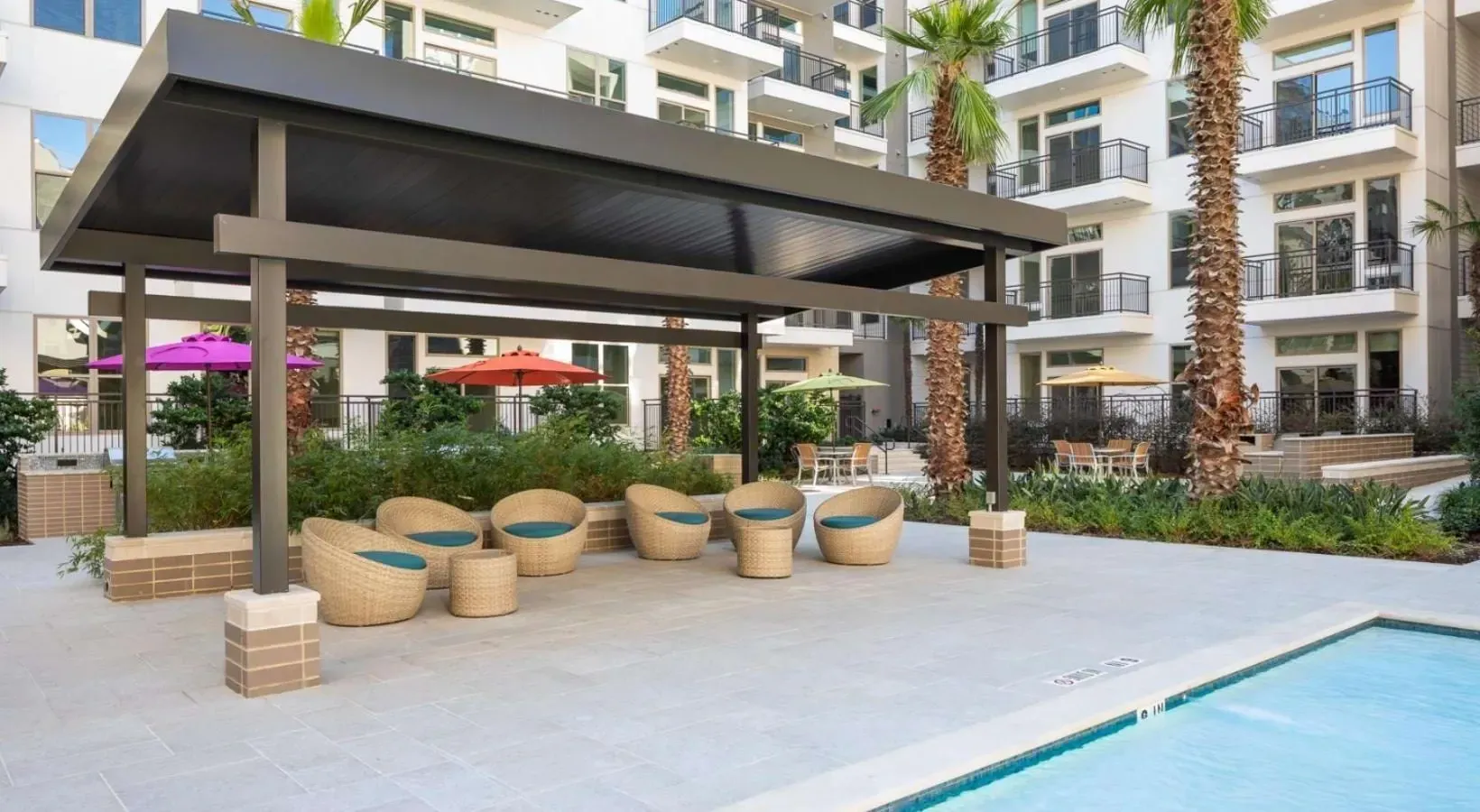 Modern outdoor lounge area with comfortable seating, umbrellas, and a swimming pool.