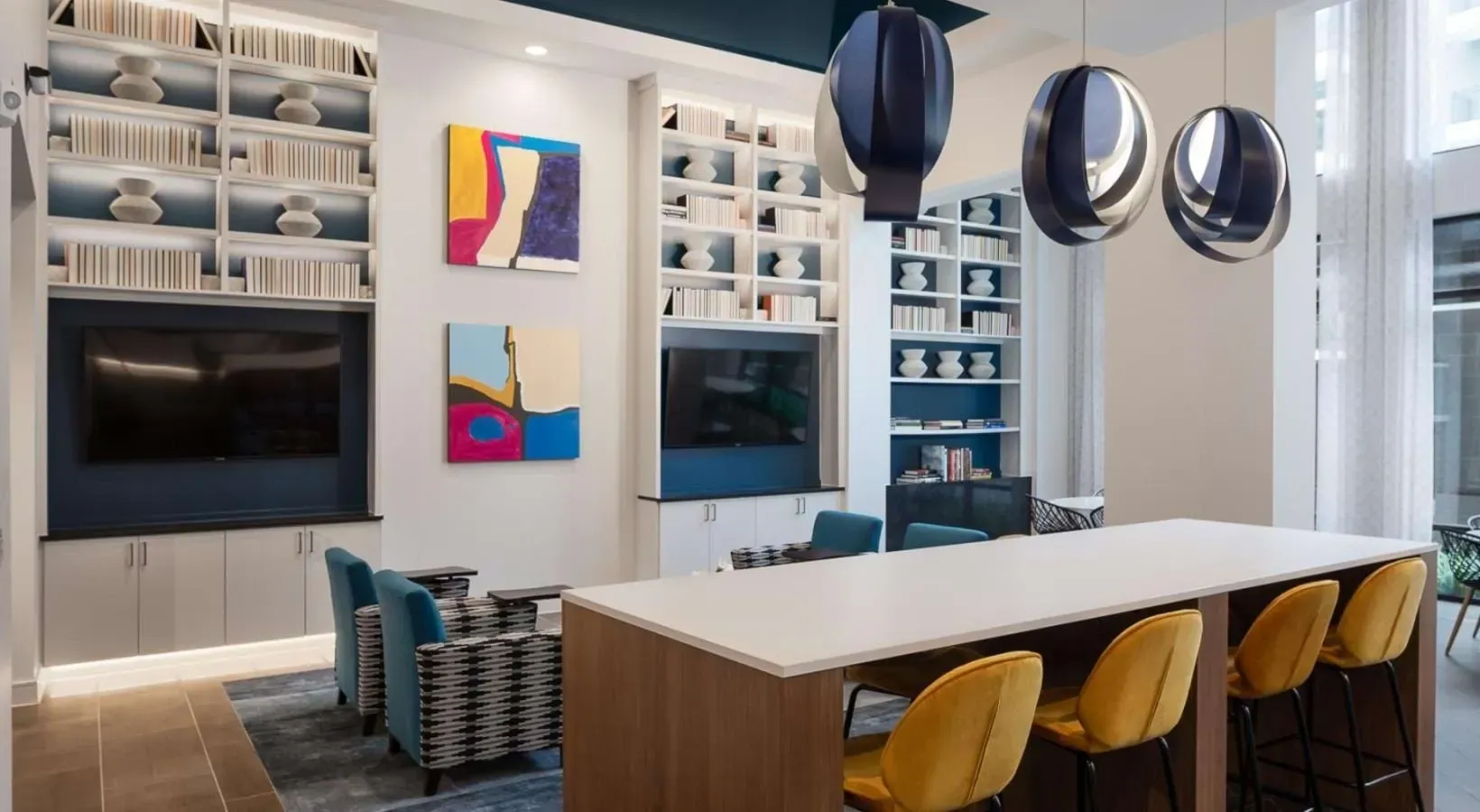 Modern communal lounge area with high-top table, accent chairs, and bookshelves.
