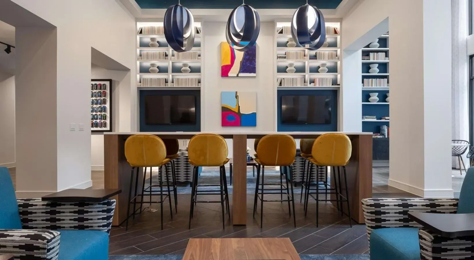 Modern lounge area with high-top bar, yellow stools, and built-in bookshelves.