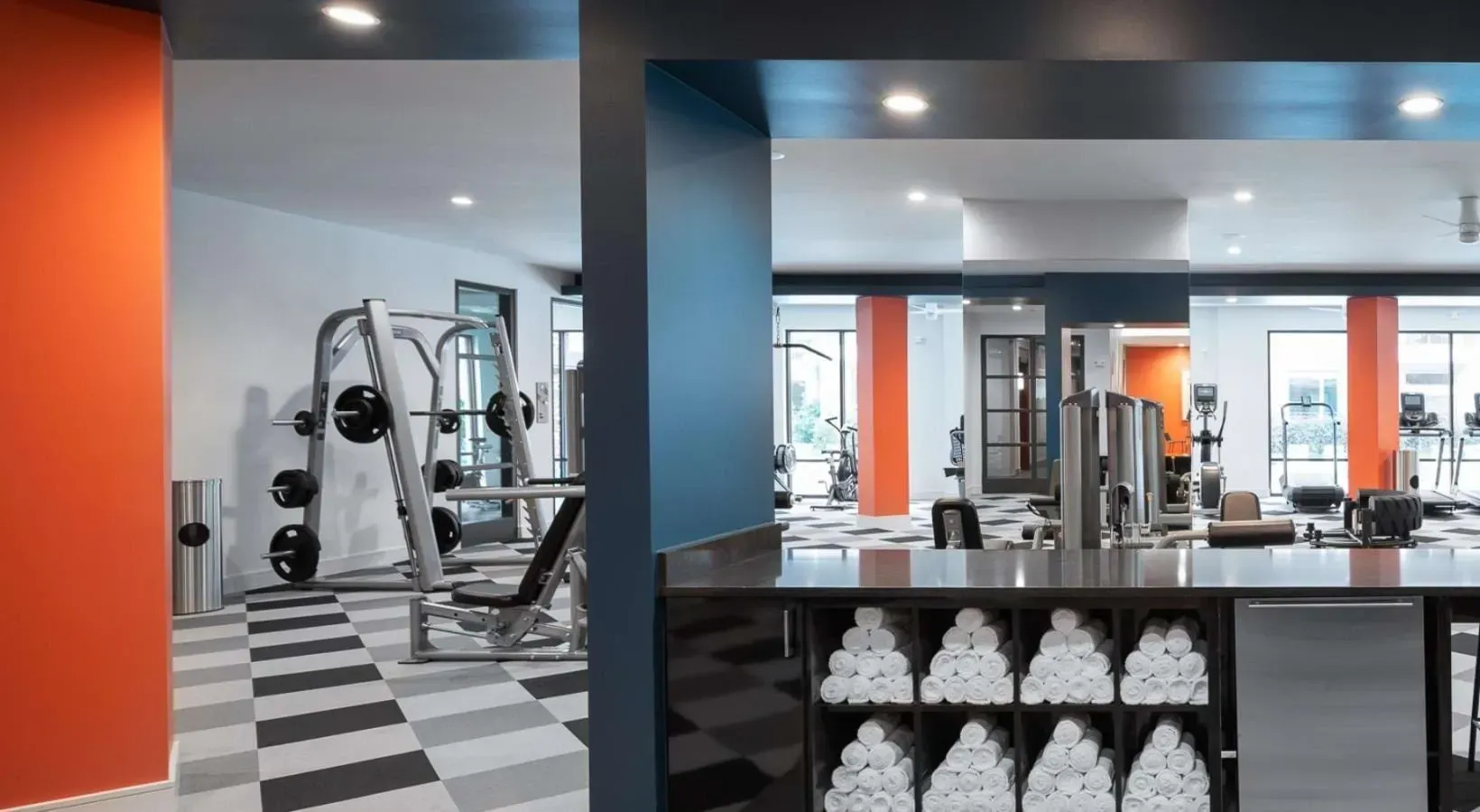 Modern apartment gym with weight racks, cardio machines, and clean towel service.