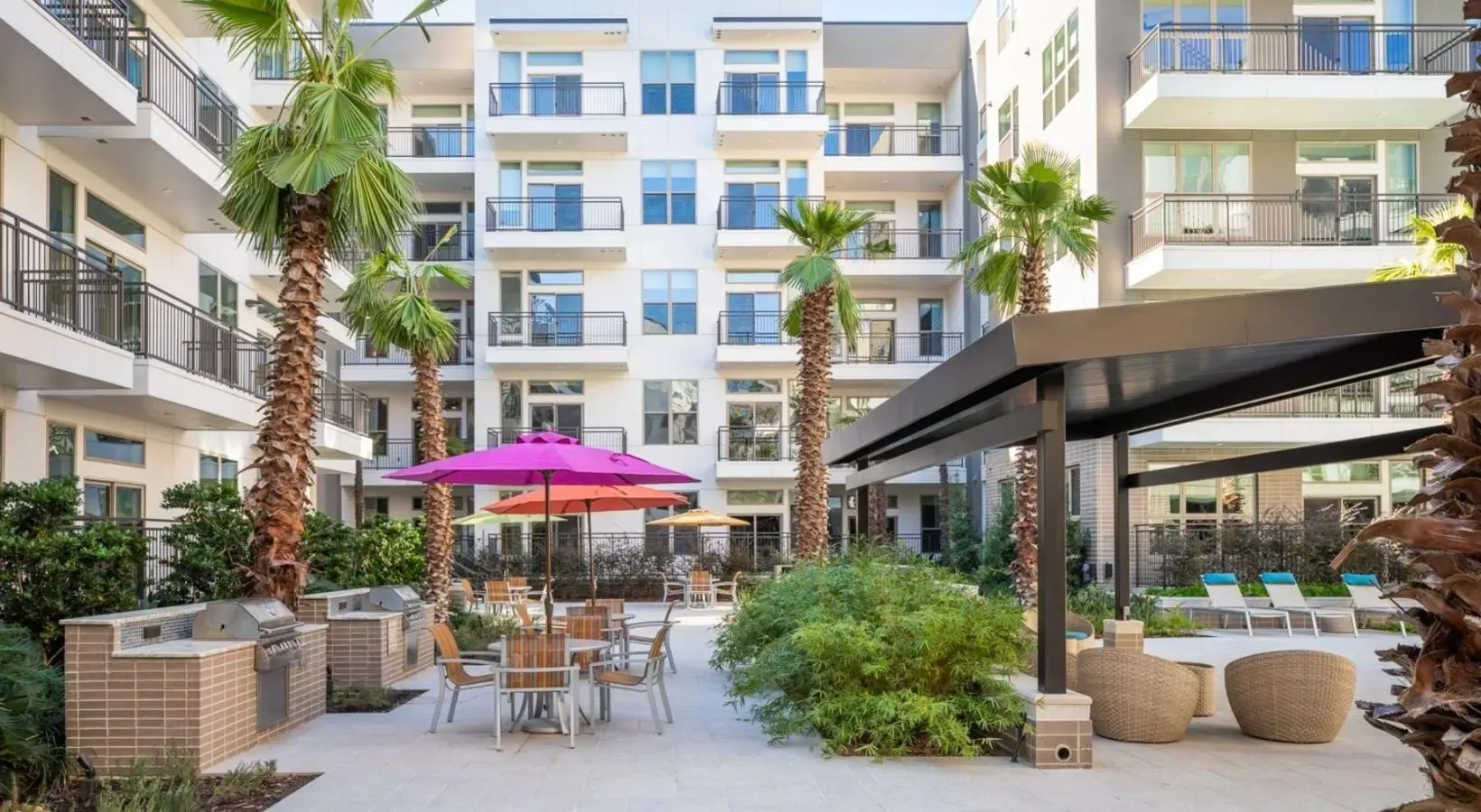 Outdoor courtyard with grills, seating, and palm trees.
