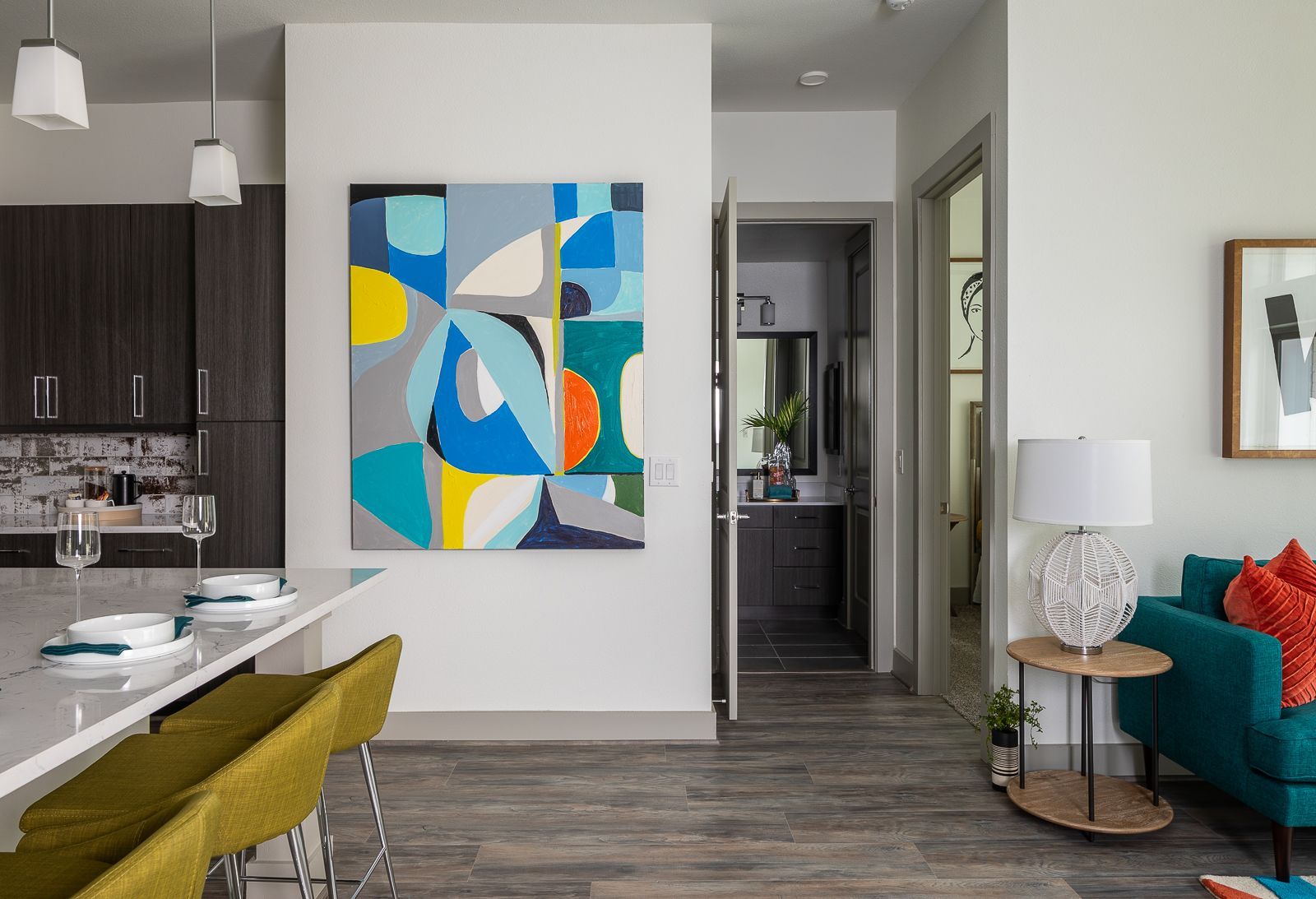 Modern open-plan apartment with abstract wall art, teal sofa, and kitchen island in view