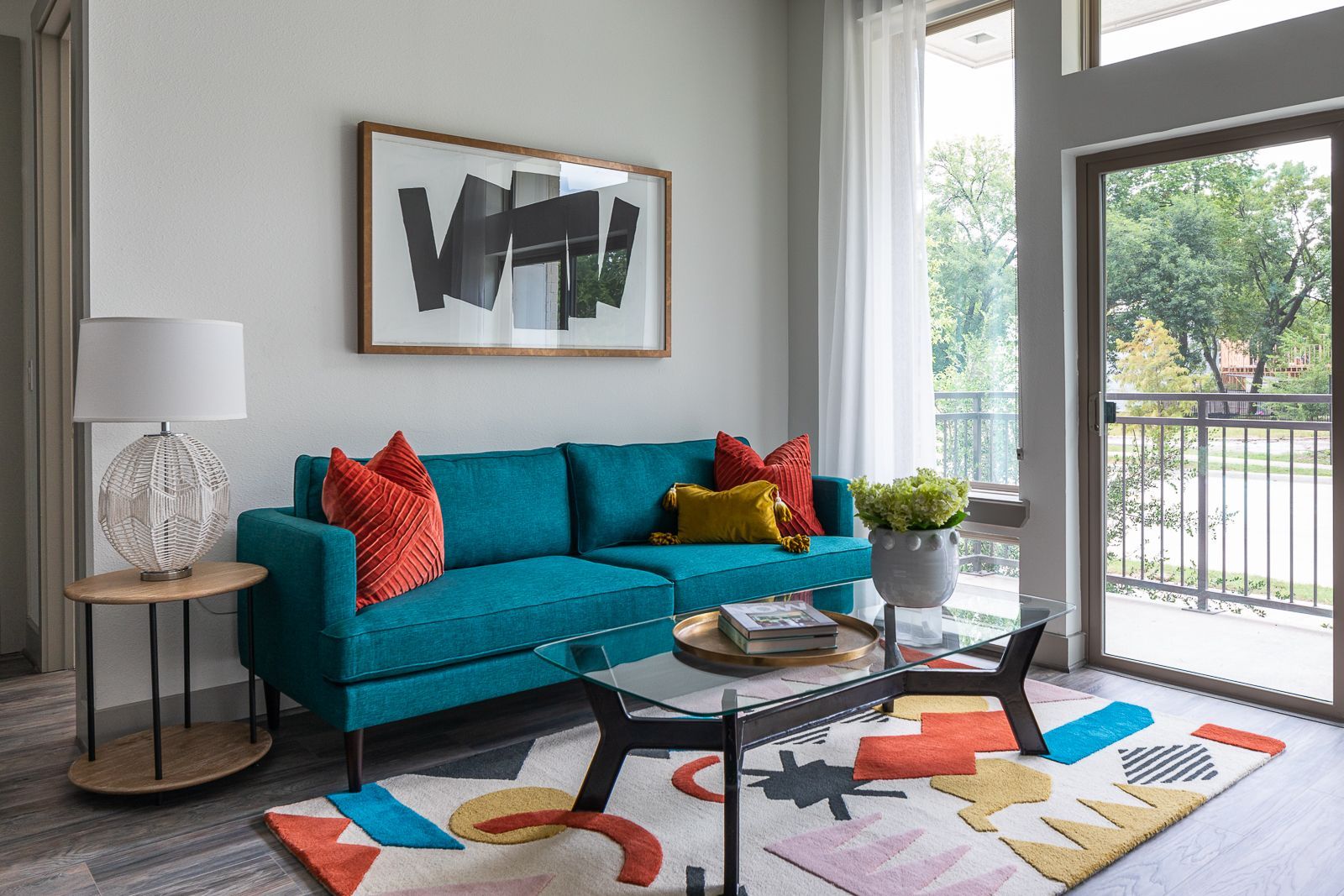 Living room with teal sofa, glass coffee table, and abstract art.