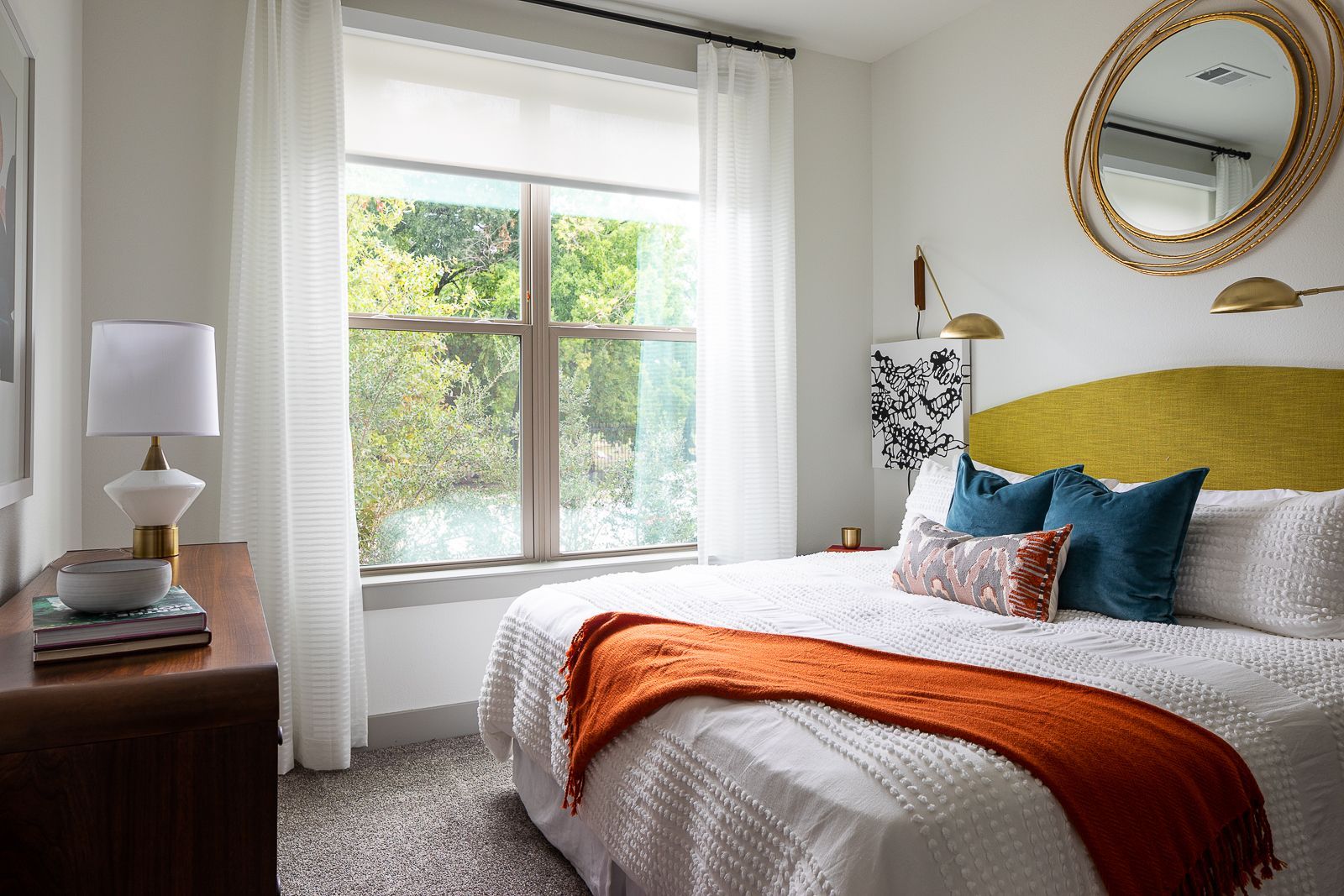 Stylish bedroom with a large window overlooking trees and a body of water.