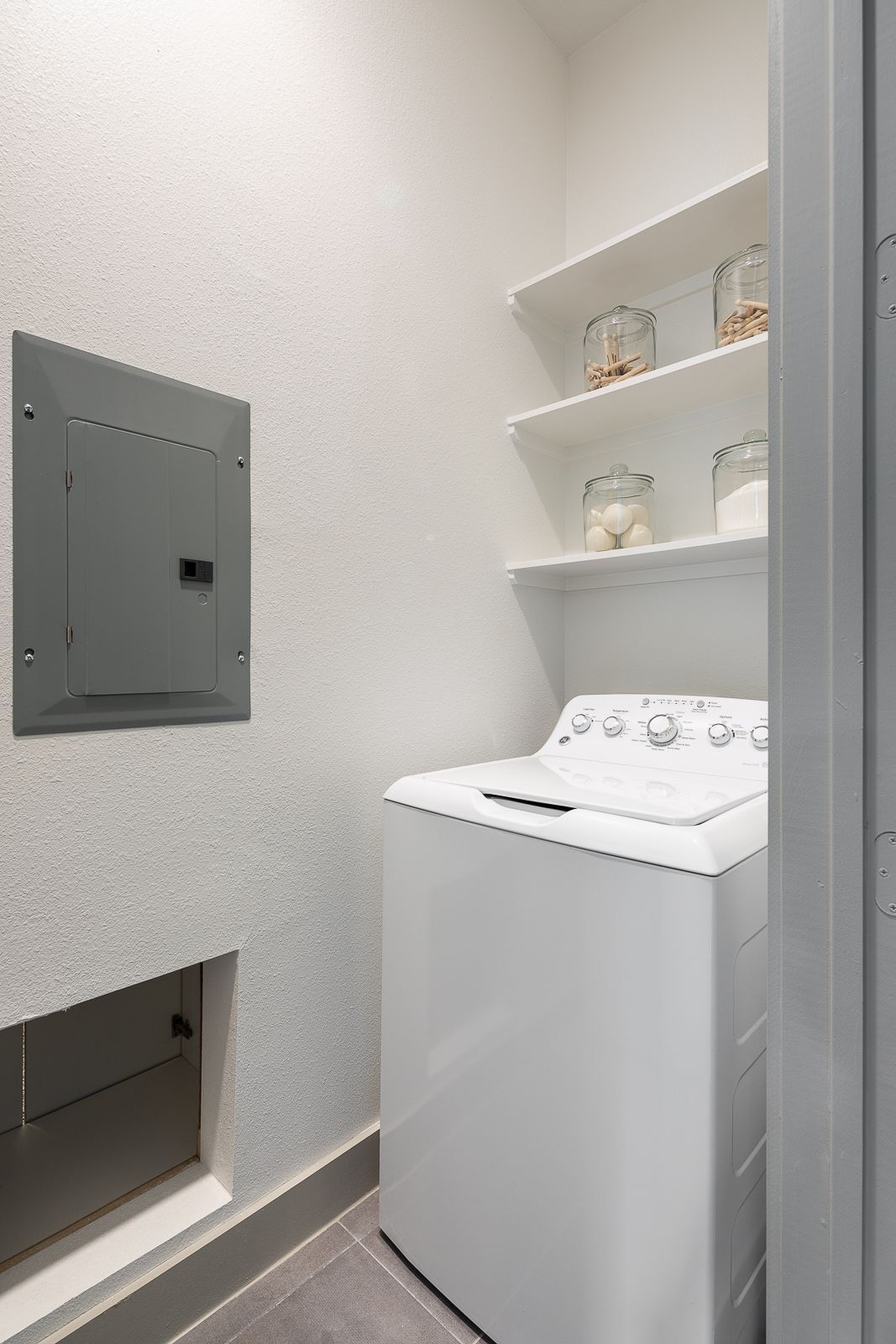 Interior laundry closet with a white washing machine and dryer, electrical panel, and storage shelves.