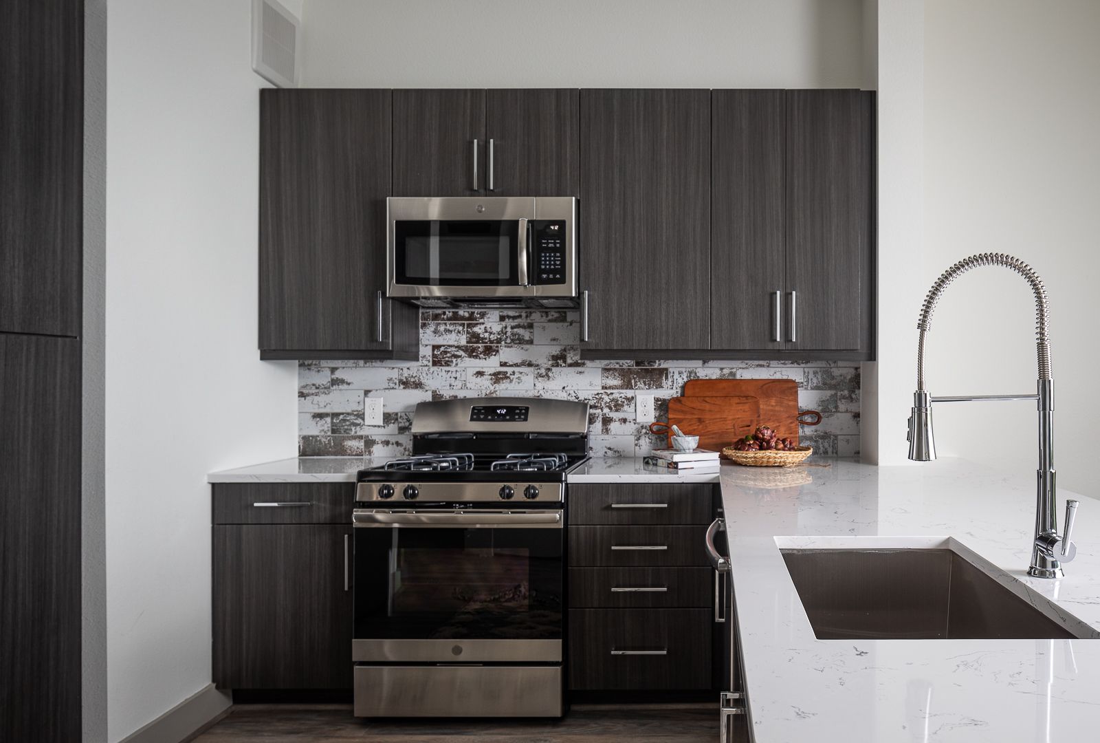 Modern kitchen with dark wood cabinets, stainless steel appliances, and a large sink.