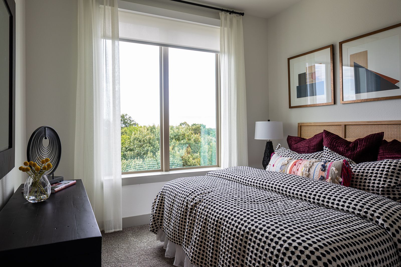 Cozy bedroom with a large window overlooking trees, featuring a queen-size bed with black and white patterned bedding.