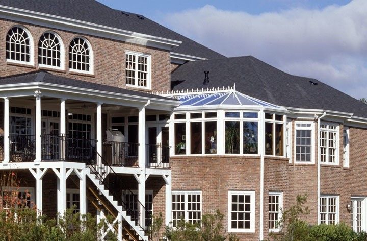 Brick house with a covered porch and sunroom featuring multiple windows under a blue sky.