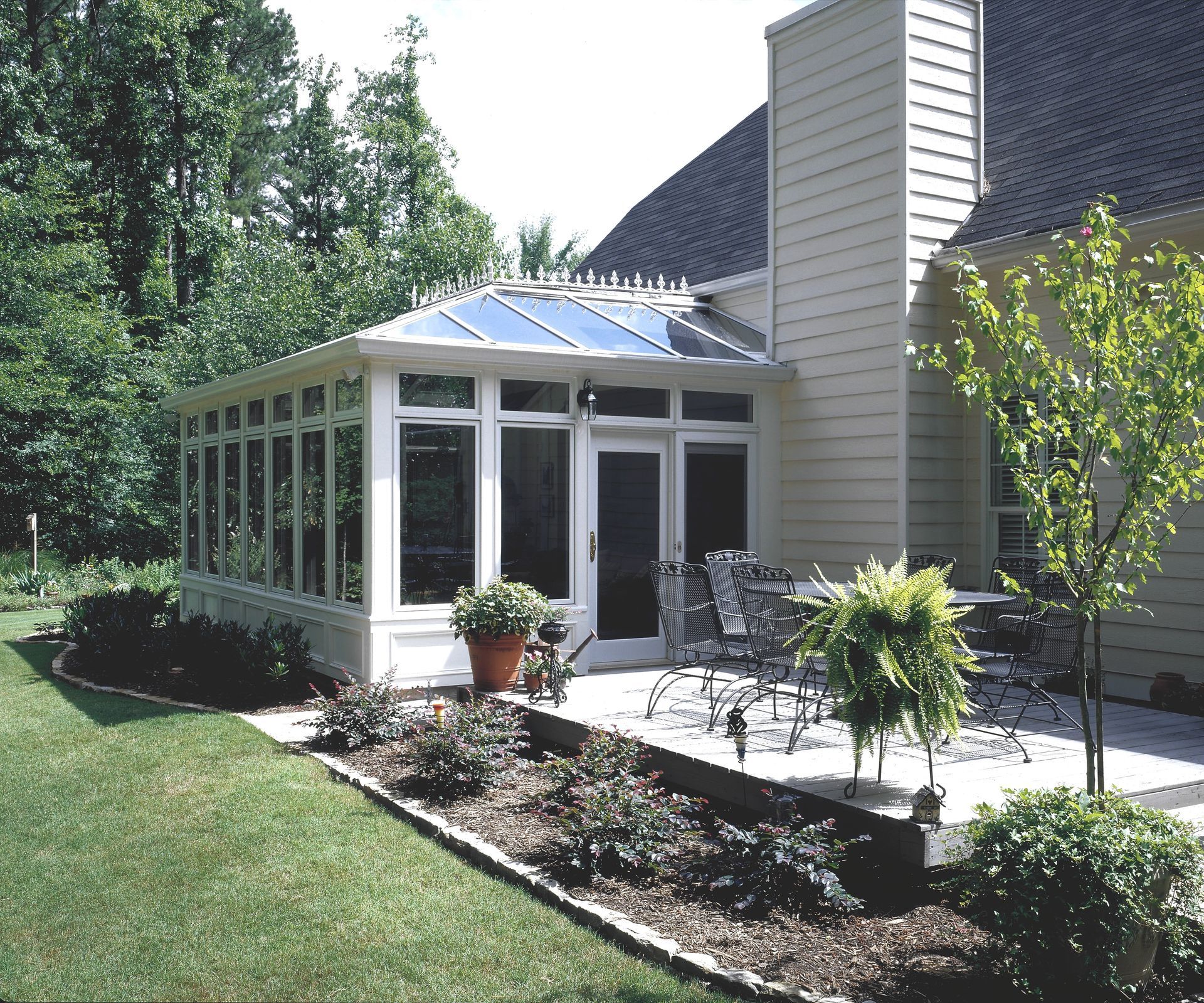 Sunroom with glass windows and doors attached to a house; patio furniture is visible.