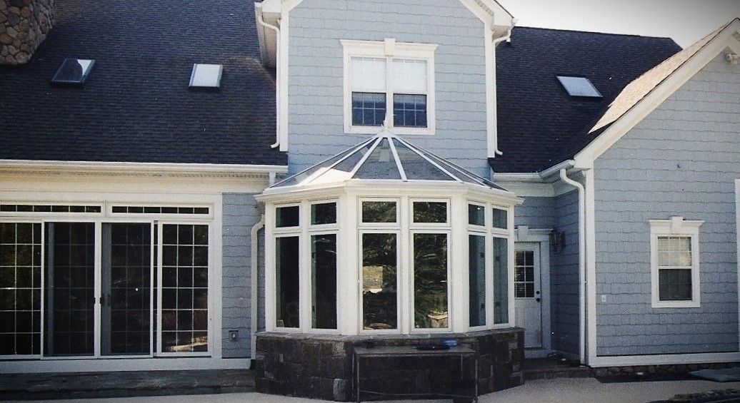 Light blue house with a sunroom, multiple windows, and a dark roof.