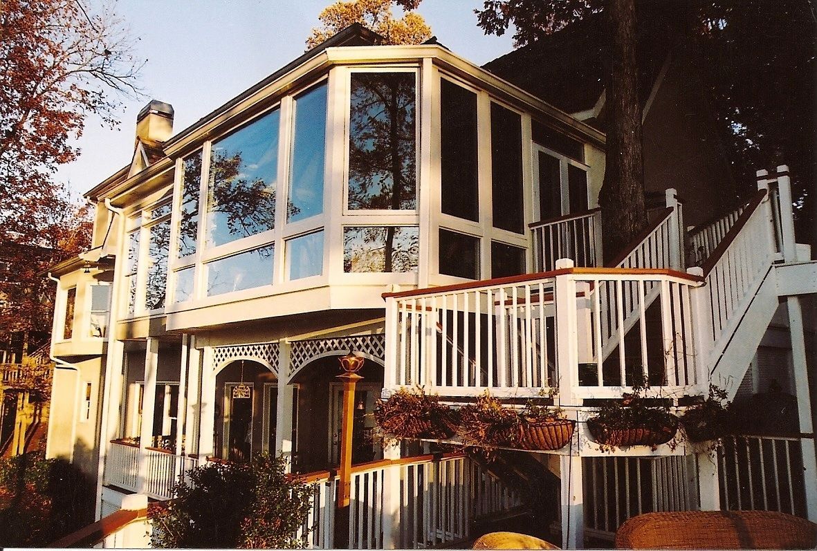 Two-story house with white trim, large windows, and a wraparound deck. A tree grows through the structure.