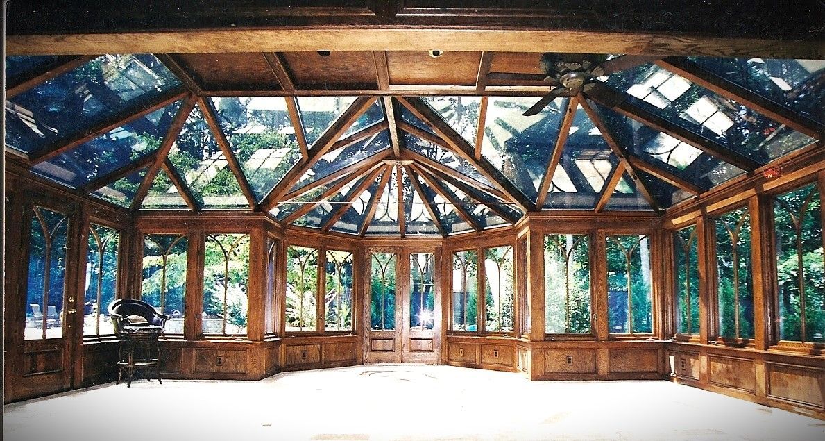 Sunroom interior with glass roof and walls, wood trim, and a door to the outside.