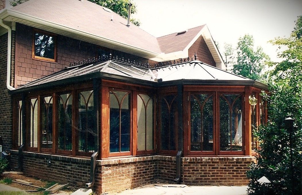 Sunroom addition with brown wood trim and brick base, attached to a brick house.