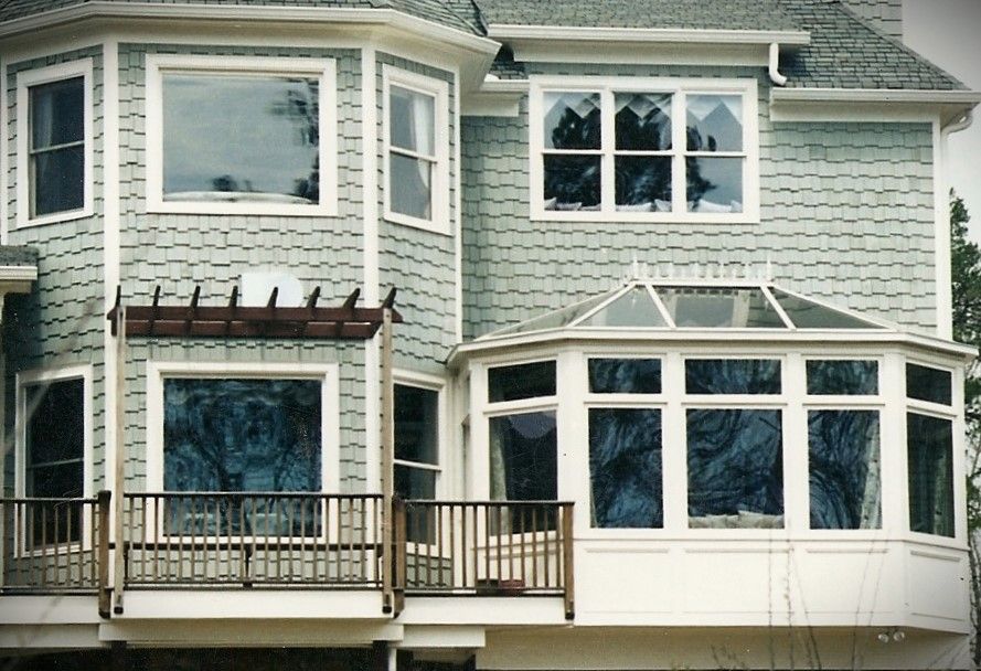 Two-story house with light blue siding, multiple windows, and a deck with a pergola.