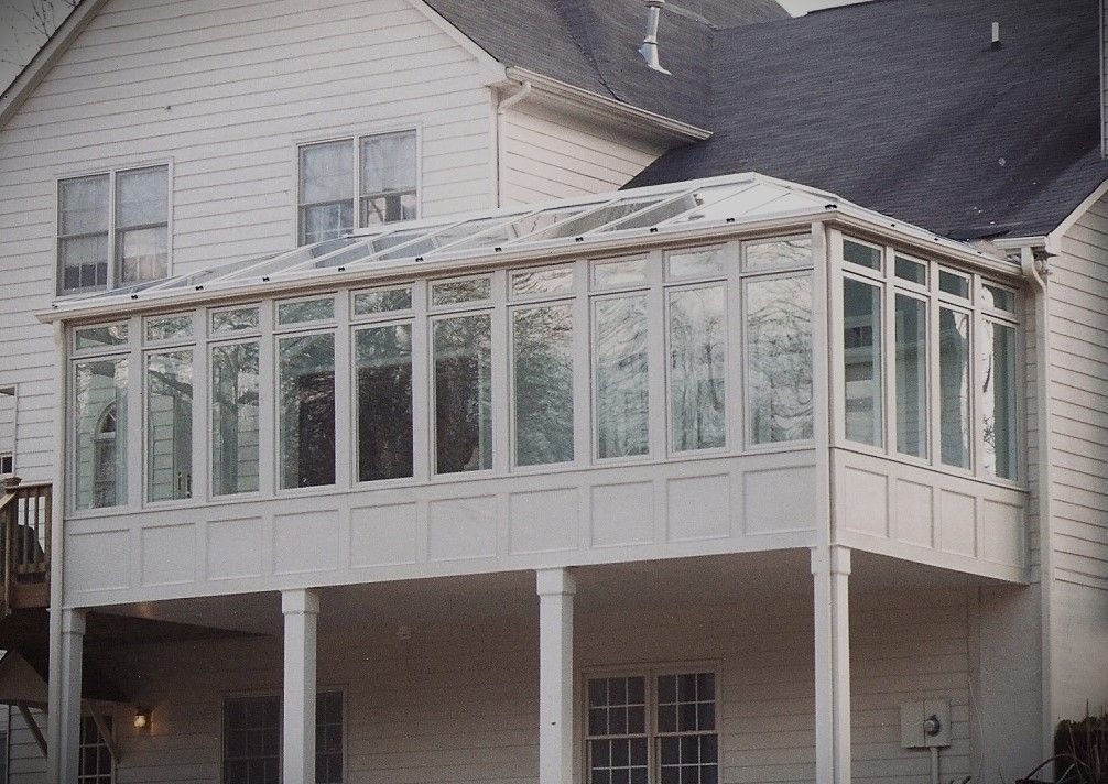 Sunroom addition to a white house with many windows and a clear glass roof.