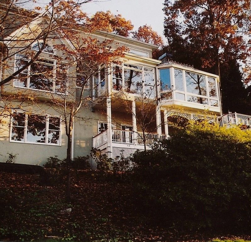 Two-story house with many windows, white trim, and a porch, set on a hillside.