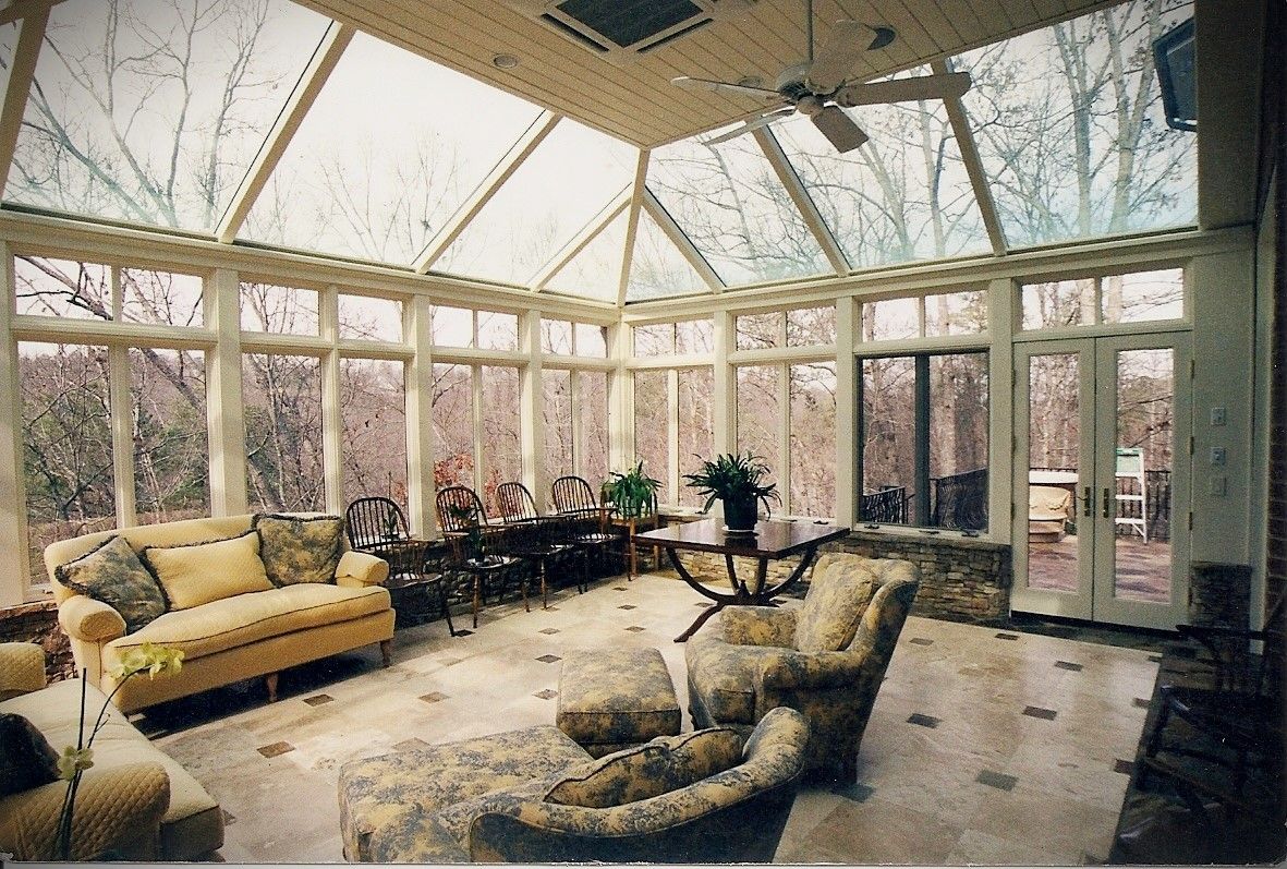 Sunroom with glass ceiling, windows, and light-colored furniture, overlooking trees.