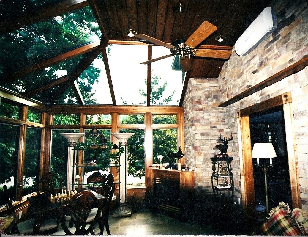 Sunroom with stone wall, wooden ceiling, and large windows looking onto trees.