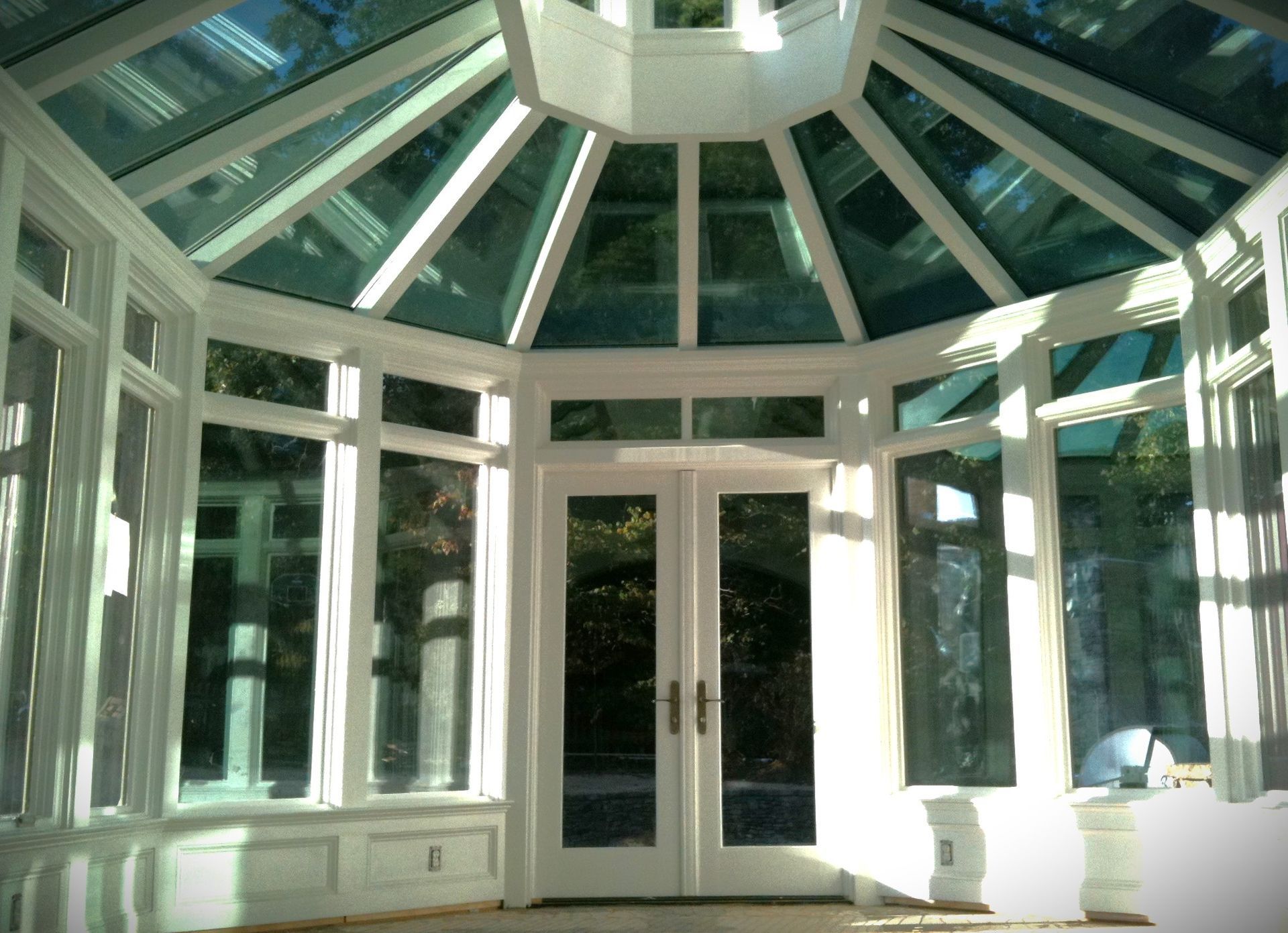 Sunroom interior with white trim, glass roof and walls, and double doors.