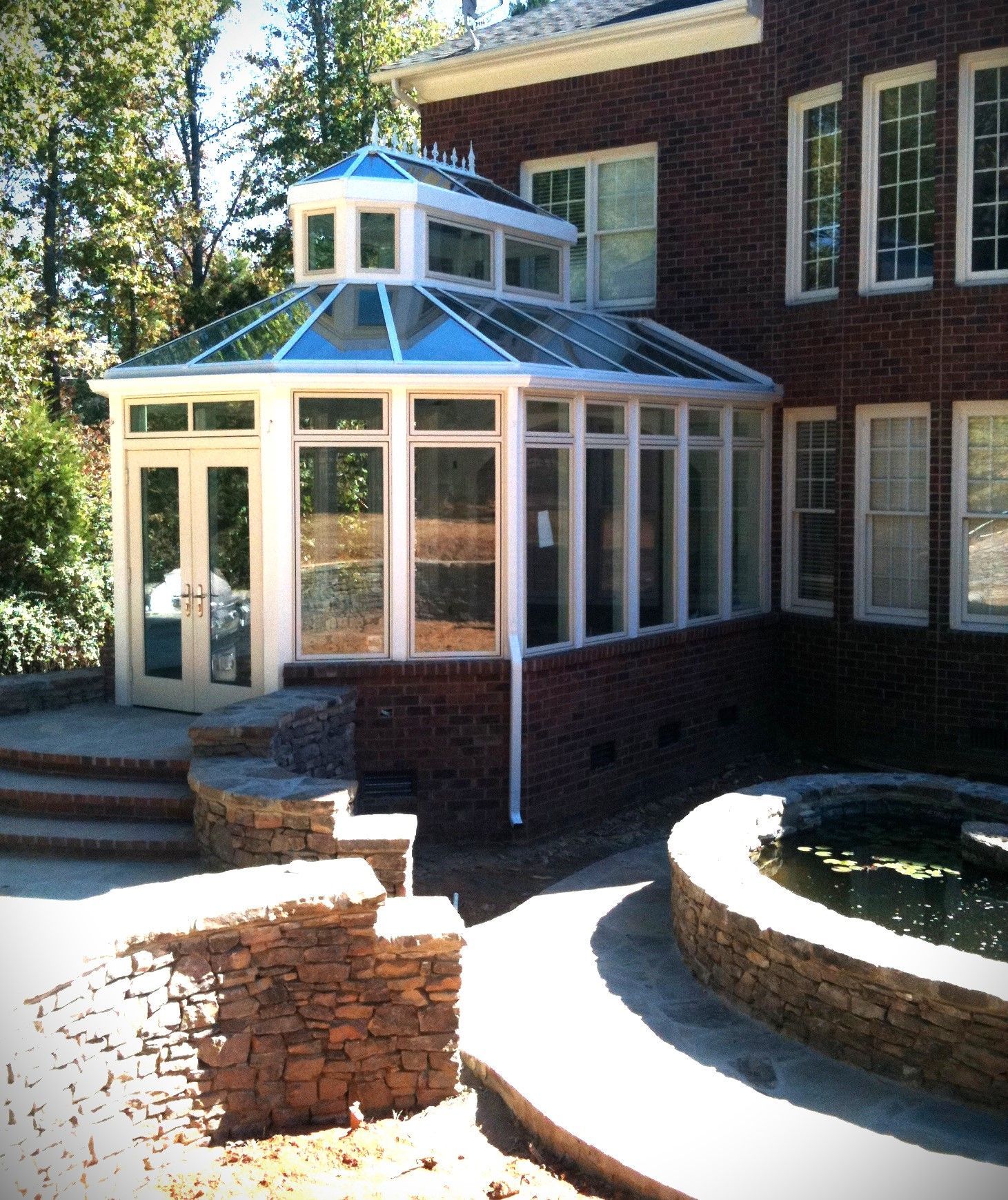 Brick house with a glass-roofed sunroom, stone patio, and a small water fountain.