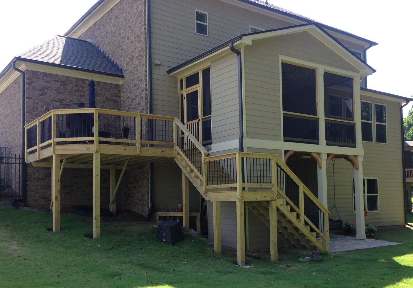 Wooden deck and screened porch attached to a two-story house with green grass in the yard.