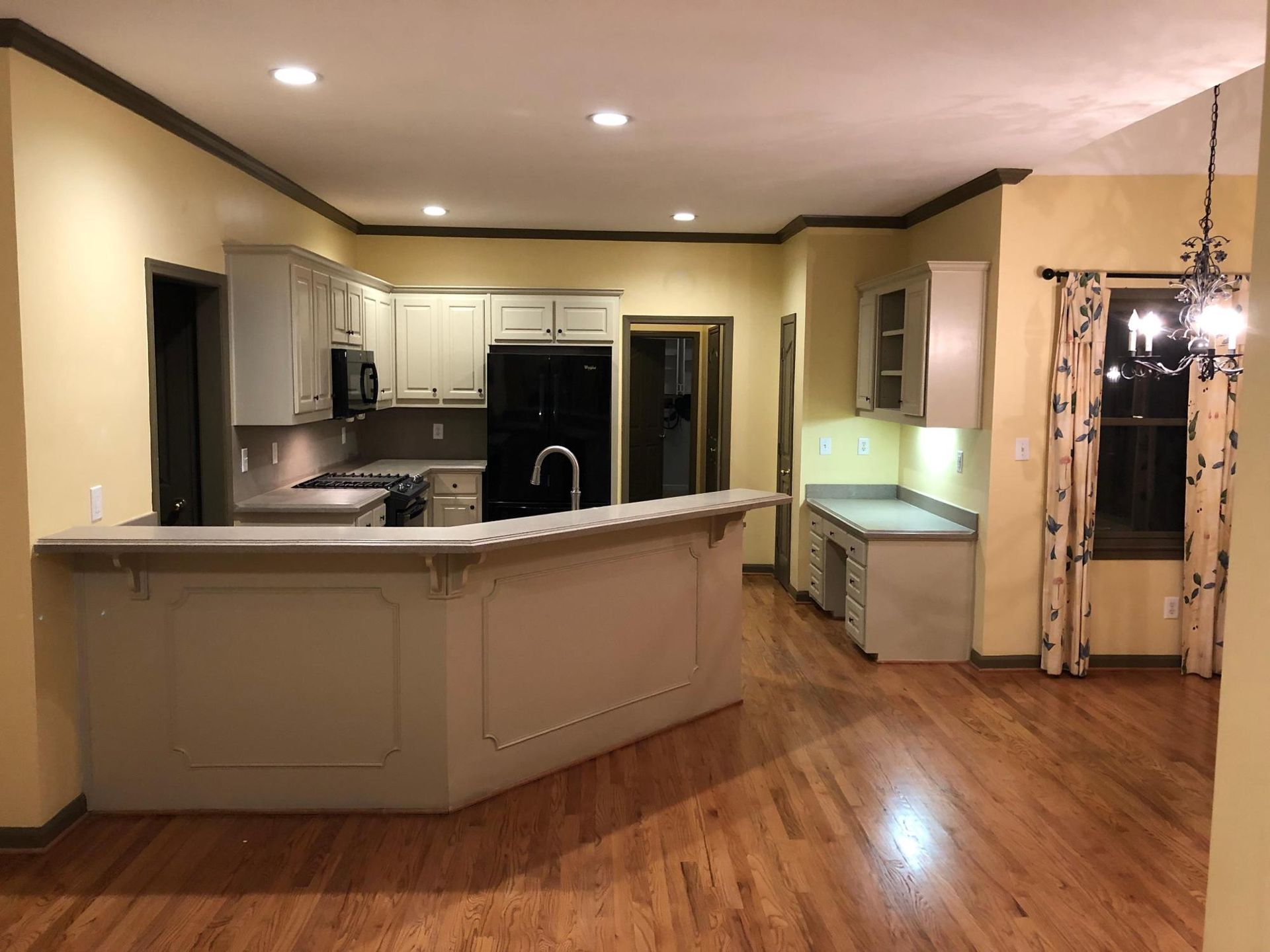 Kitchen with light-colored cabinets, black appliances, a counter, and hardwood floors.