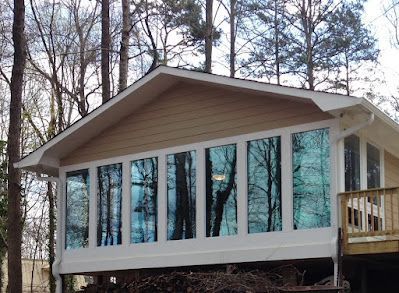 Sunroom with large tinted windows reflecting trees, beige siding, white trim, and a small wooden deck.