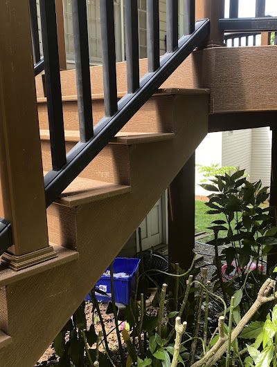Outdoor wooden staircase with black railing and steps in a yard.