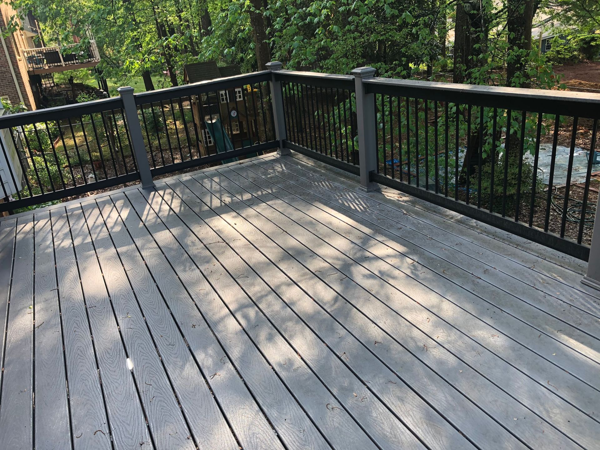 Wooden deck with gray planks and black railing overlooking trees.