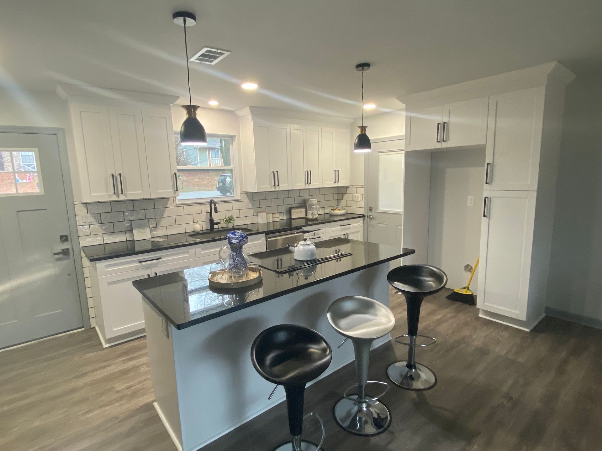 Modern kitchen with white cabinets, black countertops, island with bar stools, and pendant lights.