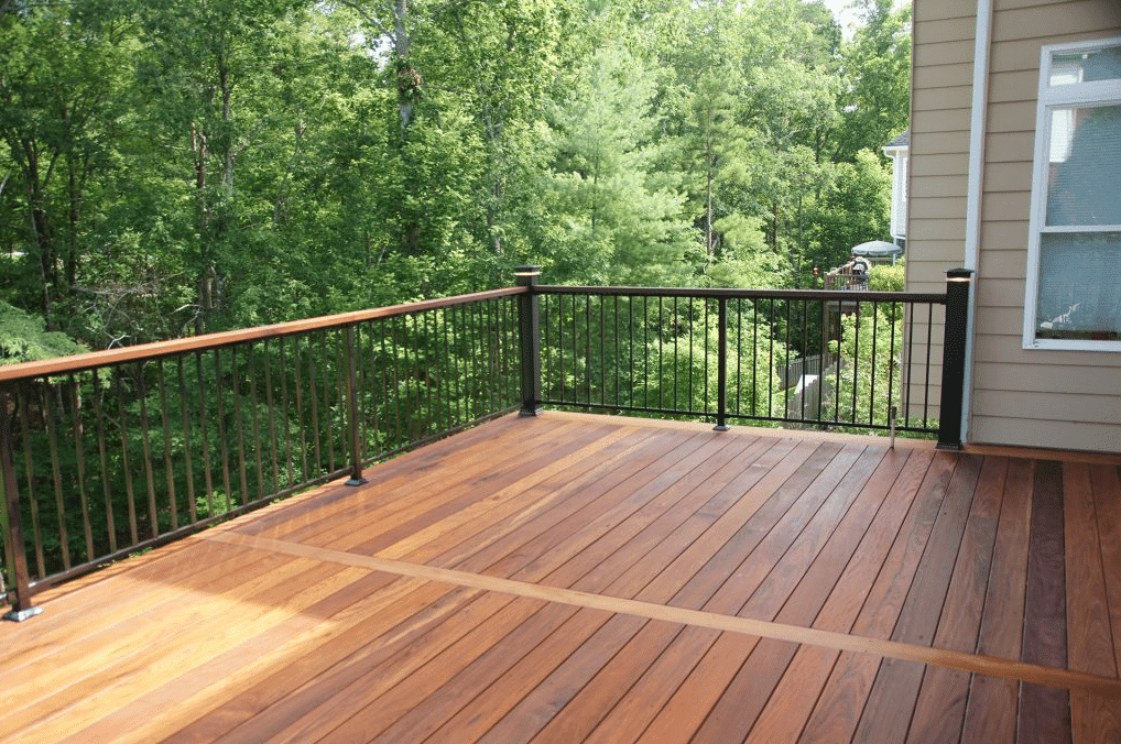 Wooden deck with black railing and lush green trees in the background.