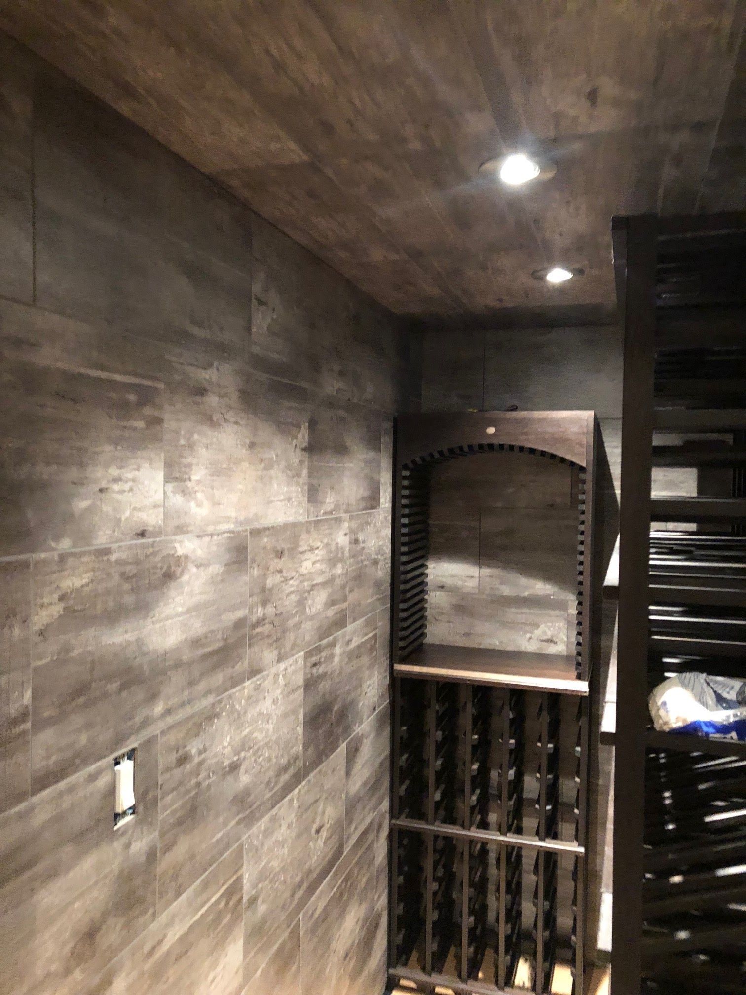 Wine cellar with dark wood-look tile walls and ceiling, recessed lights, and wine racks.